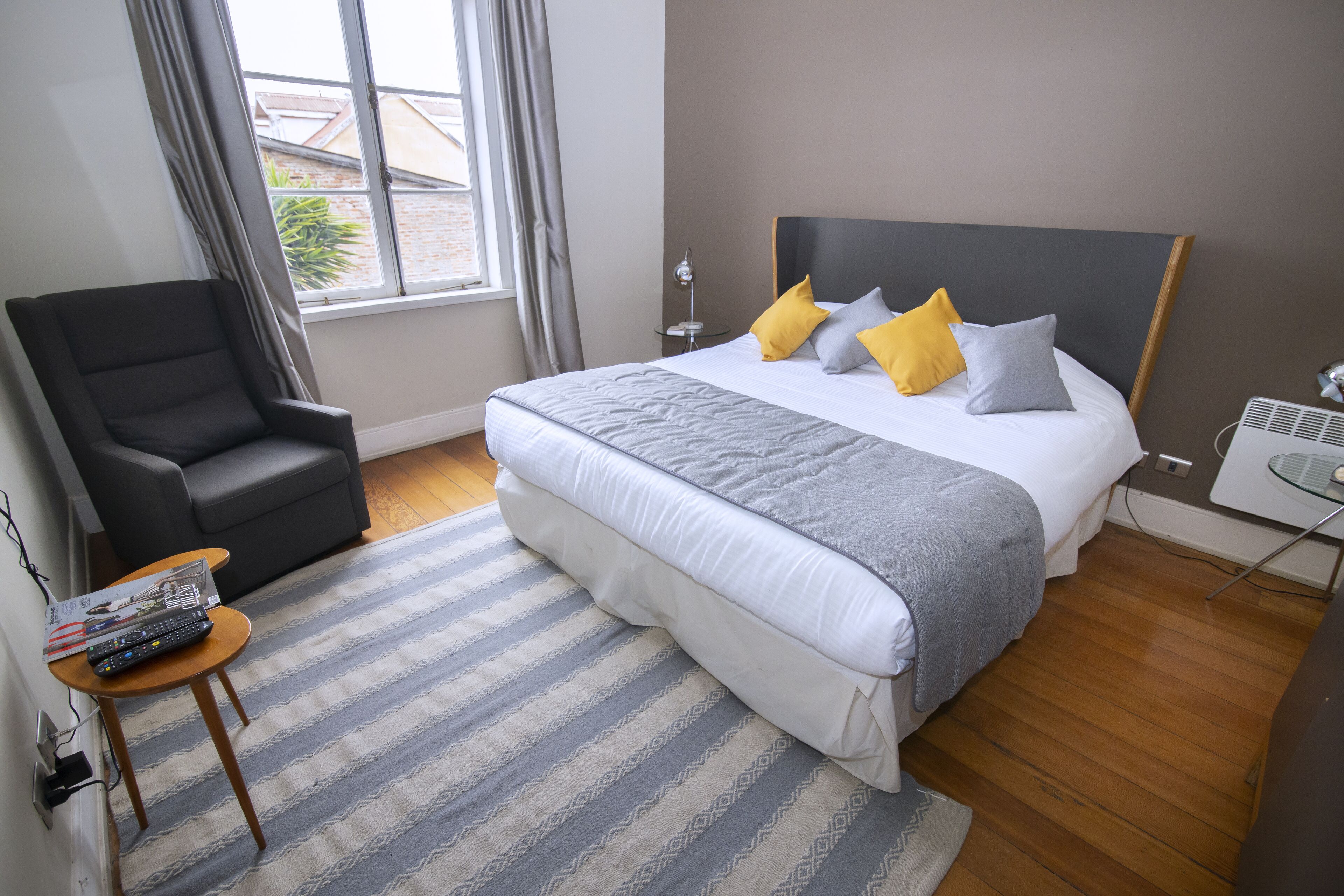 A bedroom with a large bed, a chair, a small table, and a window.