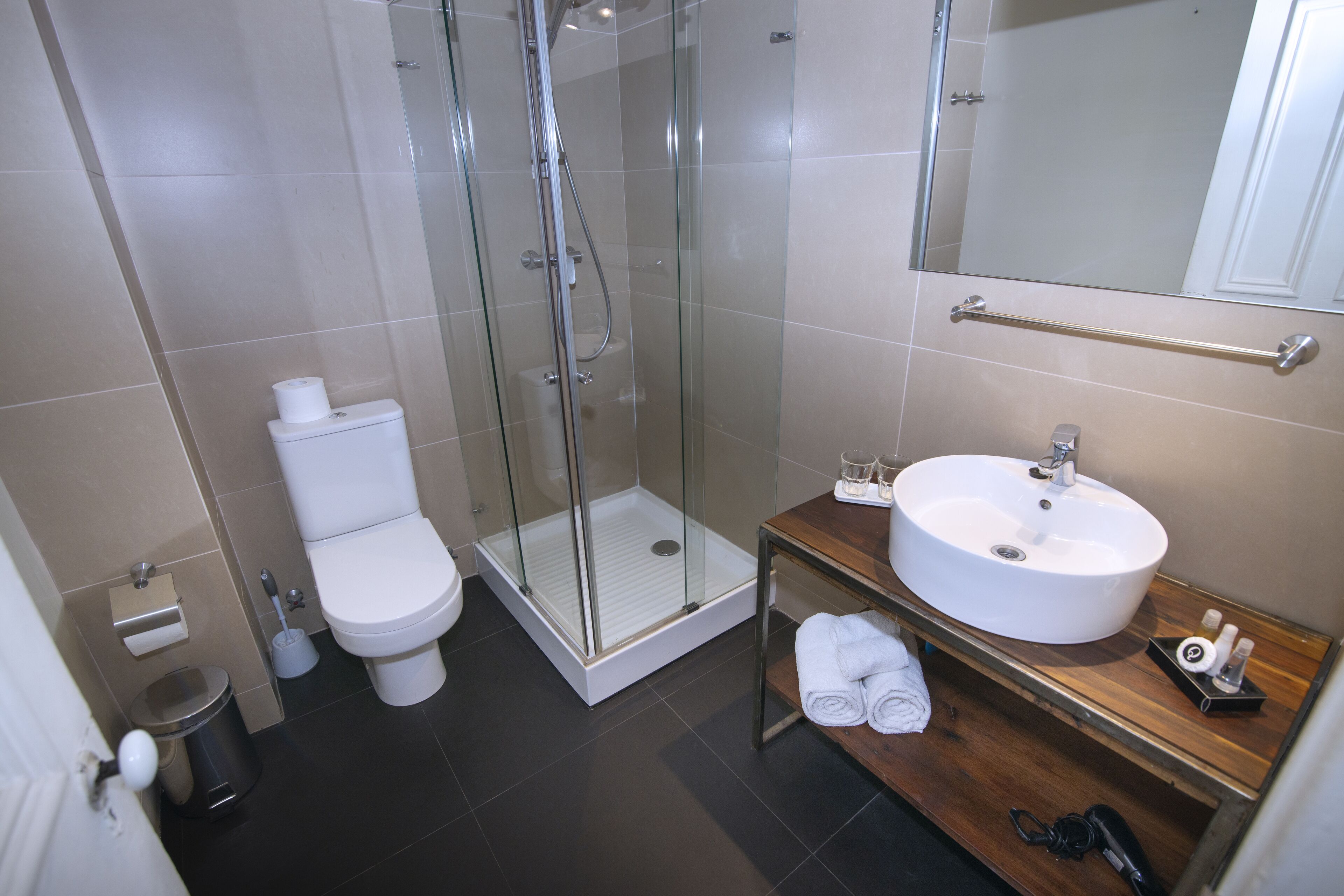 Un baño moderno con ducha envuelta en vidrio, inodoro blanco, tocador de madera con lavamanos y espejo.