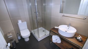 Un baño moderno con ducha envuelta en vidrio, inodoro blanco, tocador de madera con lavamanos y espejo.