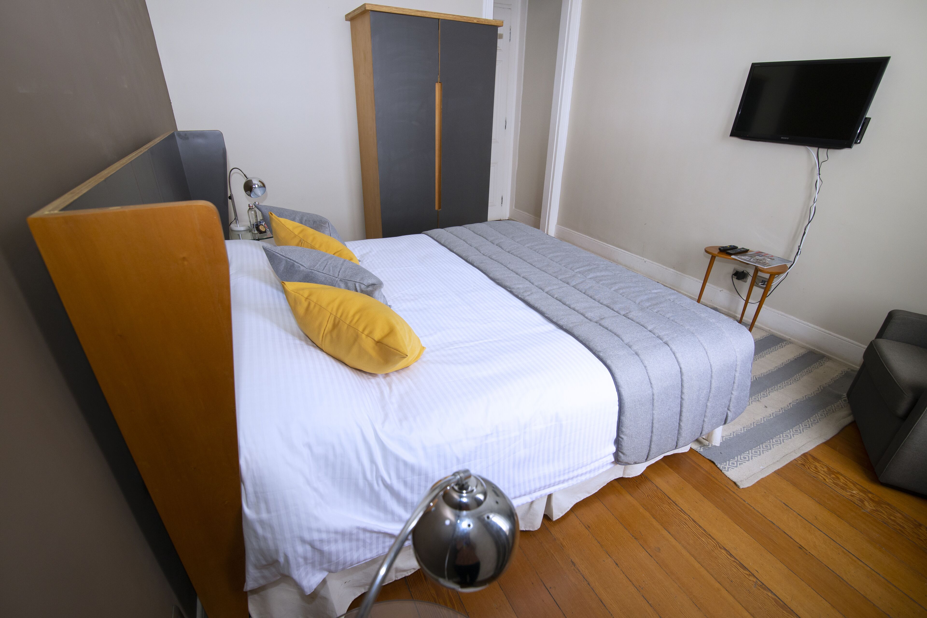 A bedroom with a bed, bedside lamp, wardrobe, TV, and a small table.