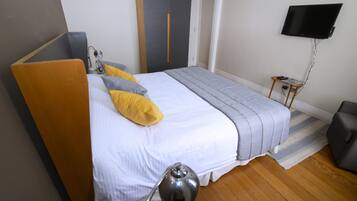 A bedroom with a bed, bedside lamp, wardrobe, TV, and a small table.
