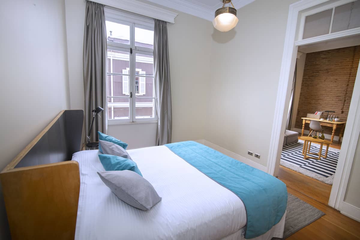 Un dormitorio con cama, ventana, escritorio y silla.