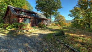 A rustic log cabin with a large front porch, surrounded by a wooded area.
