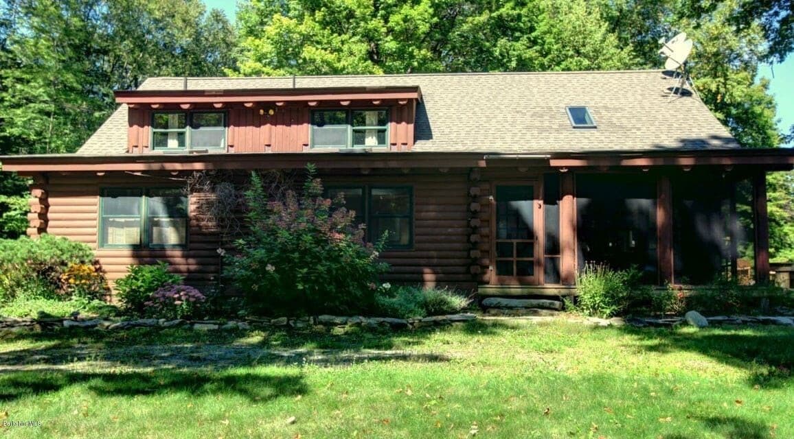 A log cabin with a front porch, a small deck, and a satellite dish.