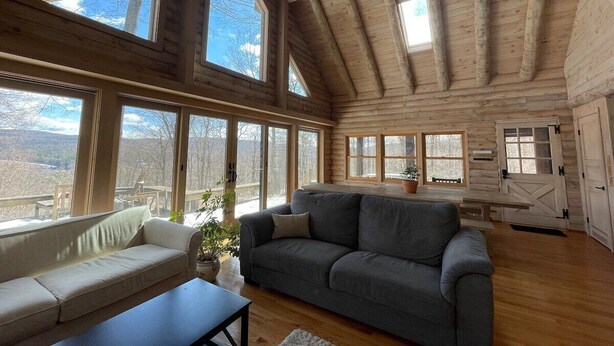 A spacious cabin with large windows, a gray sofa, and a wooden ceiling.