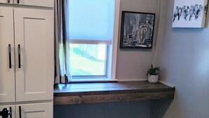 Ein Waschraum mit weißen Schränken, einem Fenster mit Jalousien, zwei Wäschekörben und einem gerahmten Bild an der Wand.