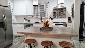 Eine moderne Küche mit weißen Schränken, einem Edelstahl-Kühlschrank, einem Einbauofen und einer Holztischinsel mit Barhocker.