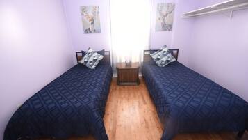 A room with two beds, wooden flooring, and artwork on the walls.