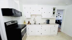 A compact kitchen with white cabinets, a black stove, and a sink. - Prime Location Duo Nest & Rest (Kingston)
