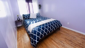 A bedroom with a bed, wooden flooring, purple walls, a window with curtains, and a small table with a plant. - Prime Location Duo Nest & Rest (Kingston)