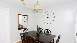 A dining room with a dark wooden table, red cushioned chairs, a wall clock, a mirror, and a chandelier. - Prime Location Duo Nest & Rest (Kingston)
