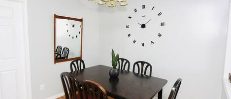 A dining area with a wooden table, red cushioned chairs, a wall clock, a mirror, and a chandelier.