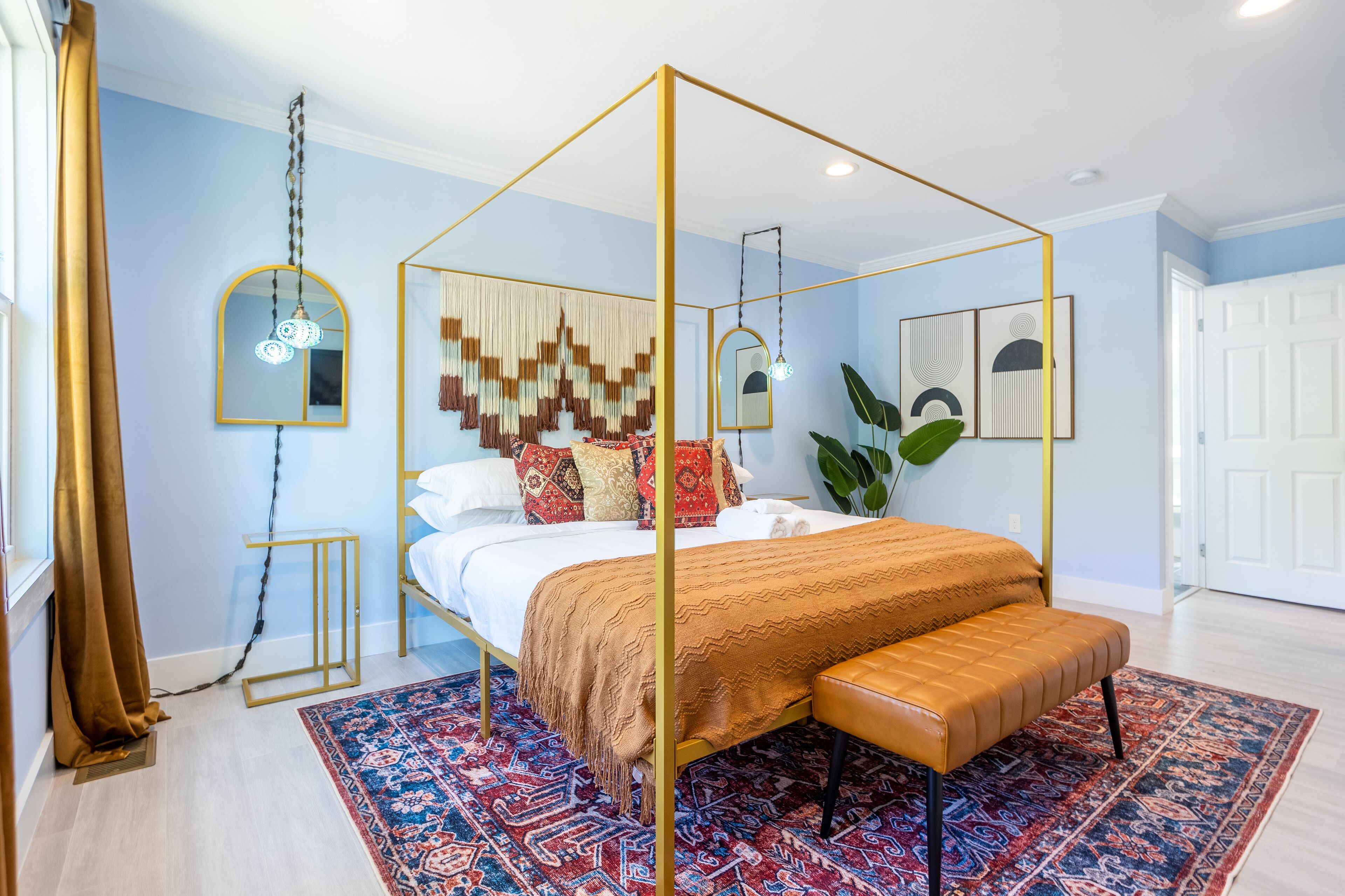 A four-poster bed with a gold frame, a patterned throw blanket, and a bench at the foot of the bed.