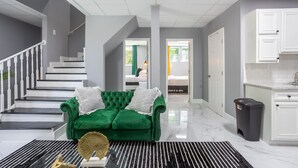A modern living room with a green velvet sofa, a black and white striped rug, and a staircase leading to another room. - Spacious Getaway 15 mins from Downtown Atlanta (Decatur)