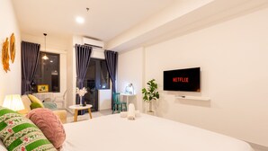 Ett hotellrum med en säng, en tv som är monterad på väggen, ett skrivbord med en stol och ett fönster med gardiner.