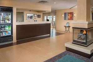 Een hotel lobby met een receptiebalie, een open haard en een koelkast gevuld met drankjes.