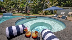 A pool area with lounge chairs, a hot tub, and a tropical garden.