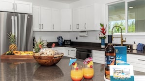A modern kitchen with white cabinets, a stainless steel refrigerator, a wooden bowl with fruits, and two glasses of orange juice.