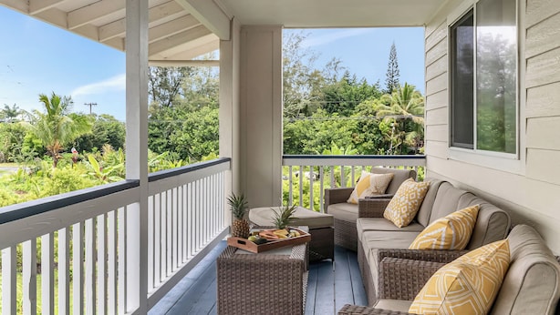 A covered porch with wicker furniture, a tray of fruit, and a view of lush greenery.