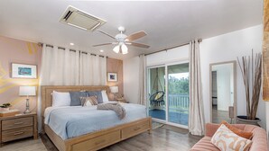 A bedroom with a bed, a ceiling fan, a nightstand, a dresser, a window, and a balcony.