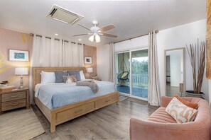 Ein Schlafzimmer mit Bett, Deckenventilator, Nachttisch, Kommode, Fenster und Balkon.