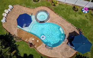 Vista aérea de una piscina con un jacuzzi circular, rodeada de sillones y sombrillas.