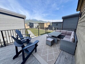 A deck with outdoor furniture, including chairs and a sofa, and a view of mountains in the background.
