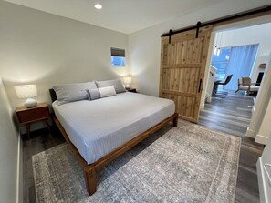 A bedroom with a bed, nightstands, a wooden wardrobe, and a view to a dining area.