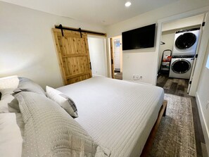 Un dormitorio con una cama, una puerta de madera, un televisor y un área de lavandería.