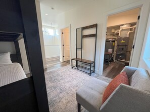 Quarto de hotel com uma cama, área de estar com um banco, um espelho grande e um guarda-roupa.