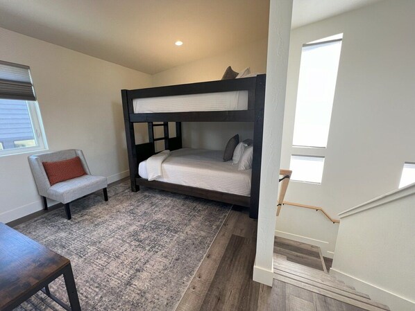 A compact room with a bunk bed, a small sofa, a wooden table, and a staircase leading to an upper level.