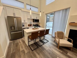 Una cocina moderna con una isla central, taburetes de bar y una zona de estar con una silla.