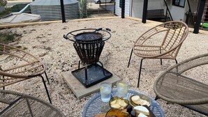 Une terrasse avec des chaises en osier, un barbecue et une table où sont disposés des en-cas et des boissons.