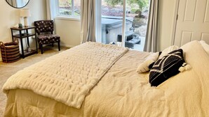 Une chambre avec un grand lit, une chaise, une petite table et une fenêtre donnant sur un jacuzzi et des arbres.