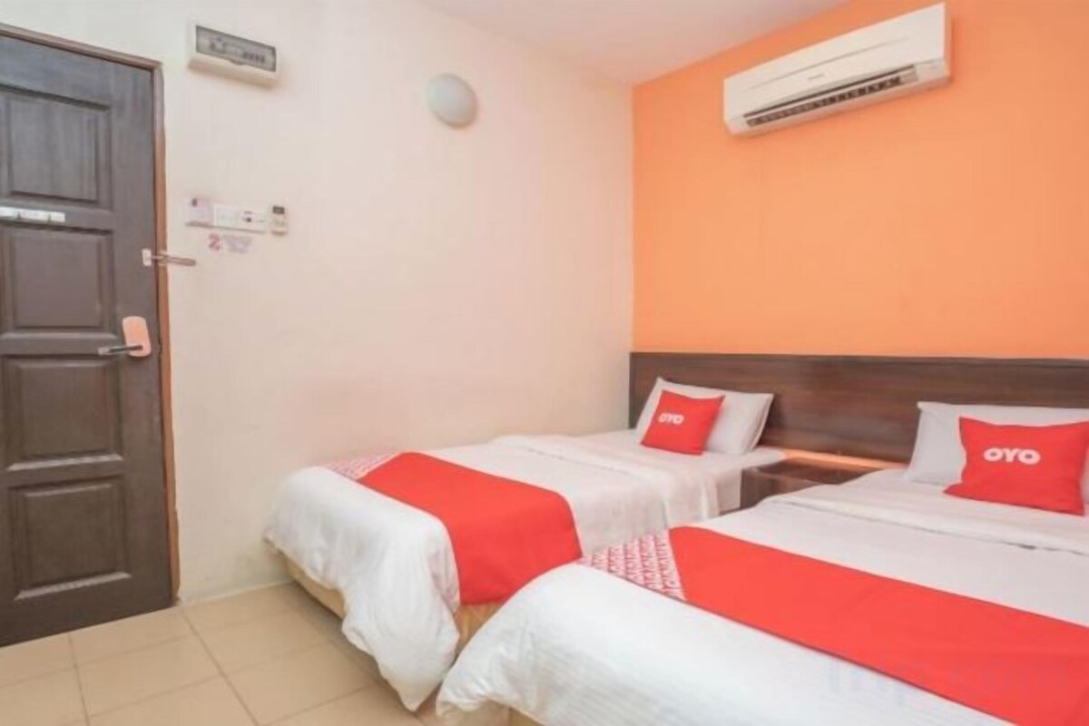 A hotel room with two beds, each with a red pillow, a wooden headboard, and an air conditioning unit on the wall.