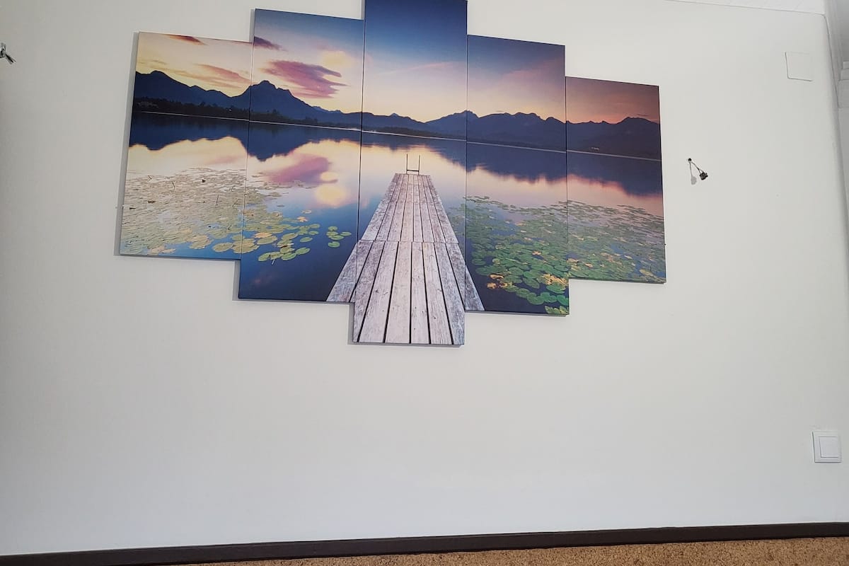 Una pared con una obra de arte de varios paneles que muestra un muelle de madera que se adentra en un lago con montañas al fondo.