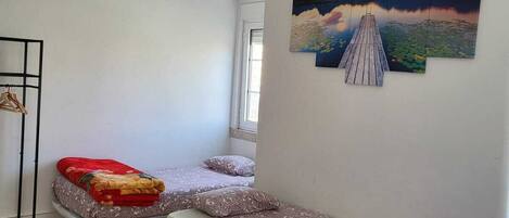 A room with two beds, a wooden floor, a painting of a lake, and a window.
