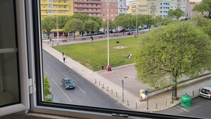 Vista desde una ventana que muestra una calle, un parque y edificios residenciales de varios pisos al fondo.