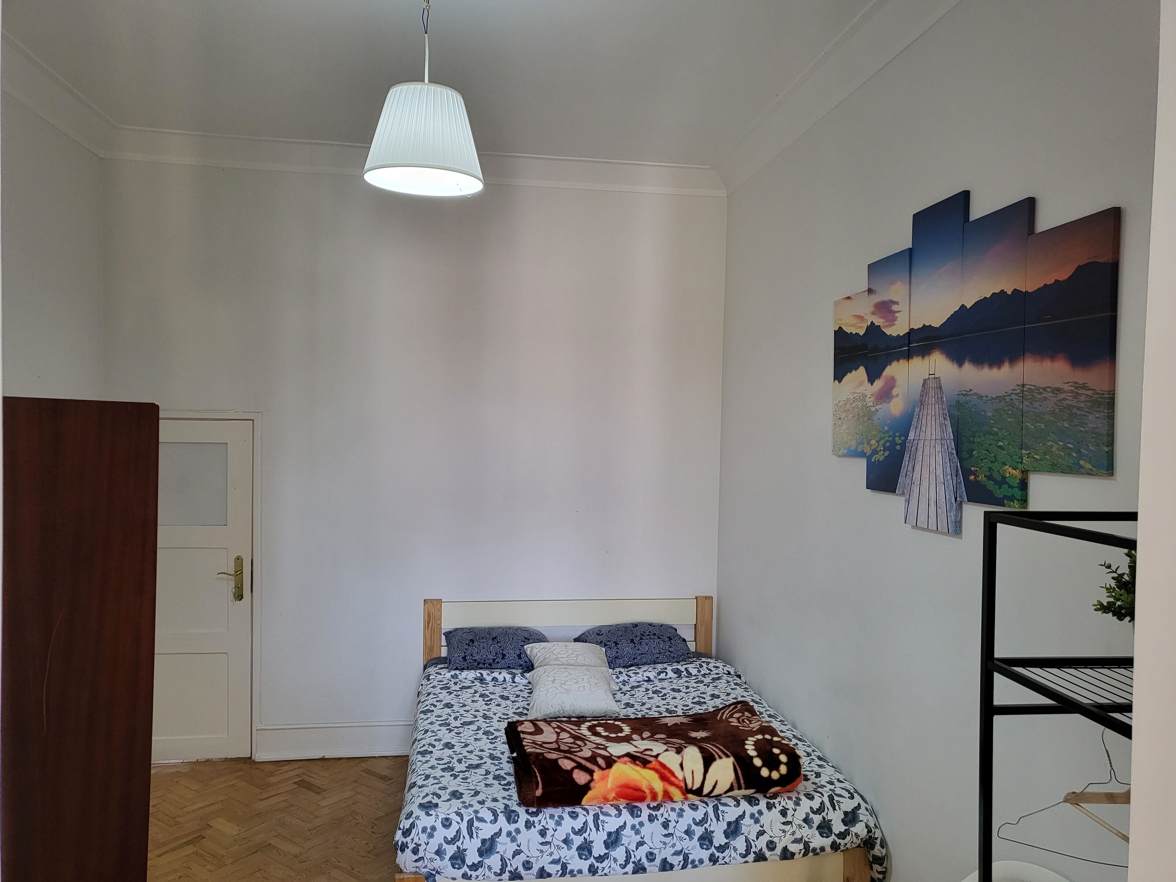 A bedroom with a bed, a hanging light, and a wall with paintings.