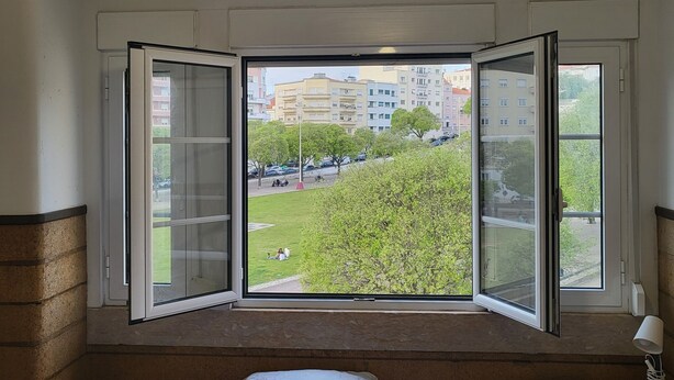 Un dormitorio con un ventanal grande, una cama con ropa de cama estampada, una mesita de noche y una lámpara colgante.