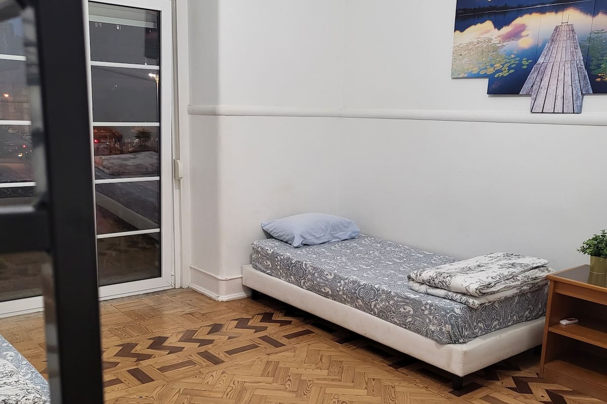 Una habitación con una cama, una mesita, un reloj de pared y un cuadro de un lago.