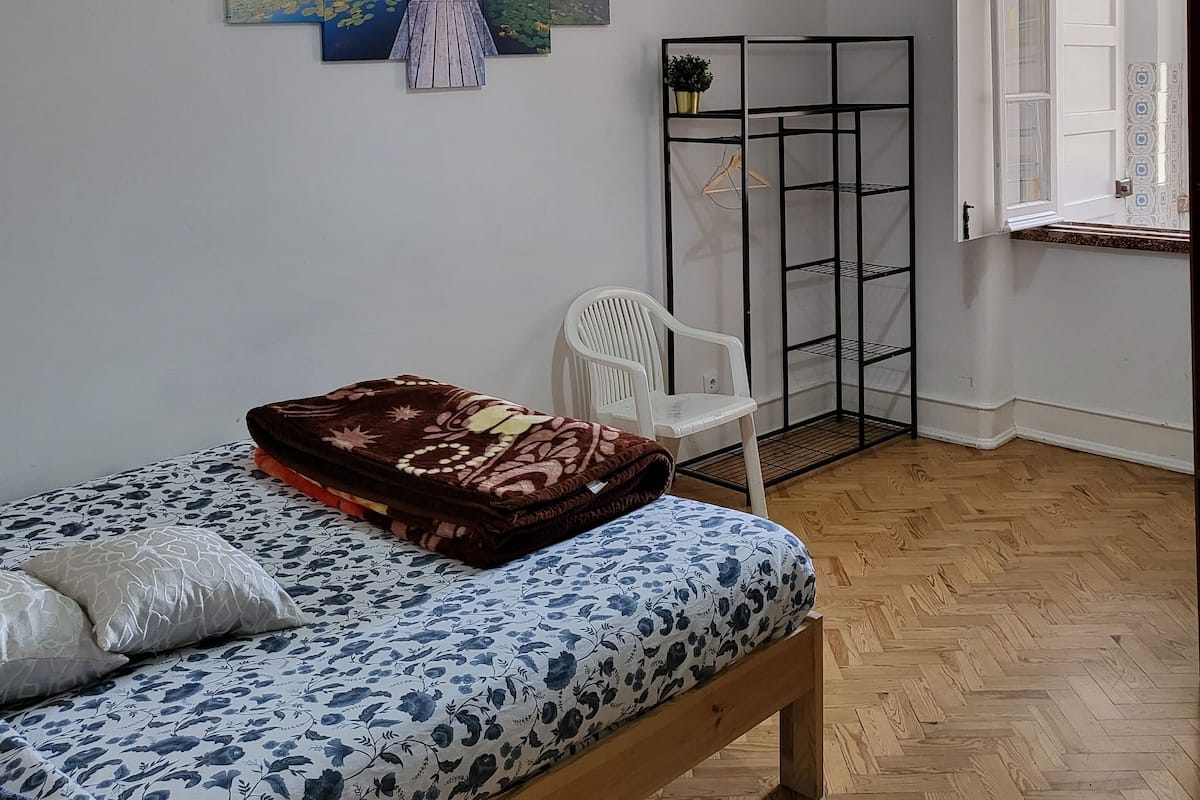 Un dormitorio con cama, una silla, un banco de madera, una lámpara colgante y un estante en la pared.