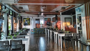 Ein geräumiges Restaurant mit Holzböden, weißen Tischen und schwarzen Stühlen. Es gibt Hängelampen und einen Deckenventilator.