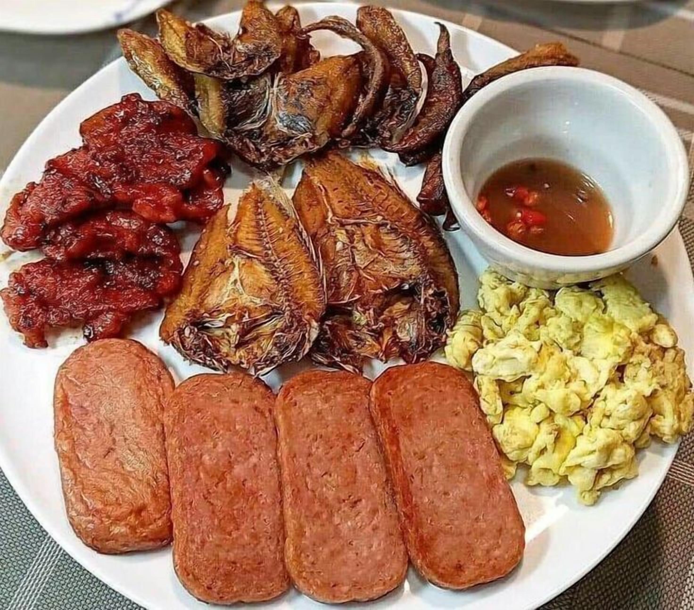 A plate with various food items including fried fish, sausages, and a bowl of sauce.