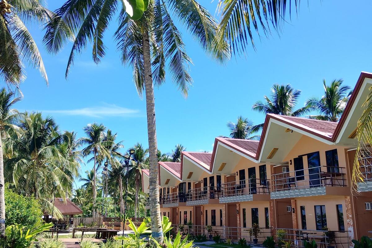 A resort with multiple two-story buildings, a well-maintained lawn, and palm trees.