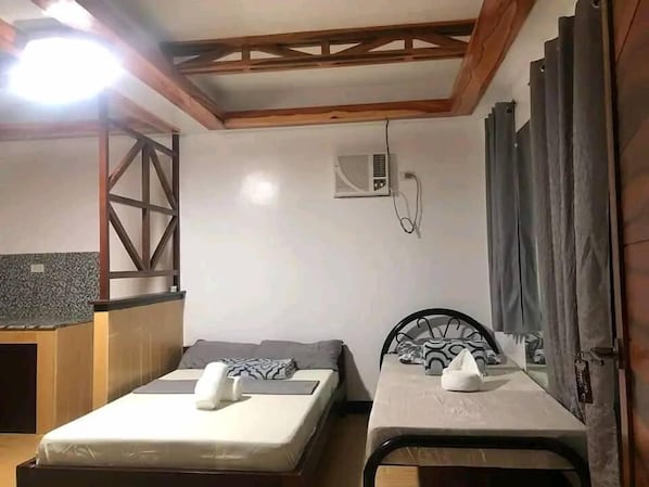 A bedroom with two beds, a wooden ceiling, an air conditioning unit, and a small kitchenette area. - LANGOJON JIANJOY RESORT (General Luna)