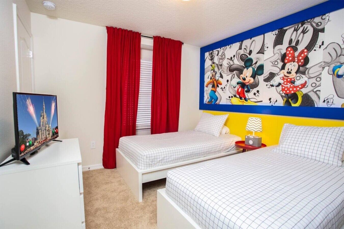 Ein Hotelzimmer mit zwei Betten, einem Fernseher, einem Wandgemälde und roten Vorhängen.