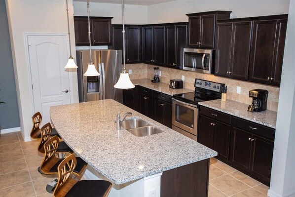 A modern kitchen with granite countertops, stainless steel appliances, and dark cabinetry.