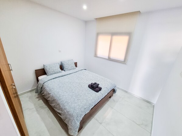 A bedroom with a bed, pillows, a window, and a door. - Sea Bay Apartment (Larnaca)