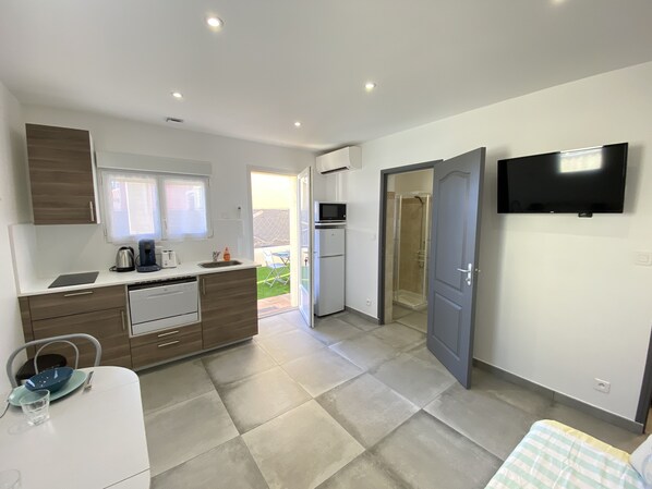 A compact kitchen with a microwave, toaster, and sink. A TV is mounted on the wall.